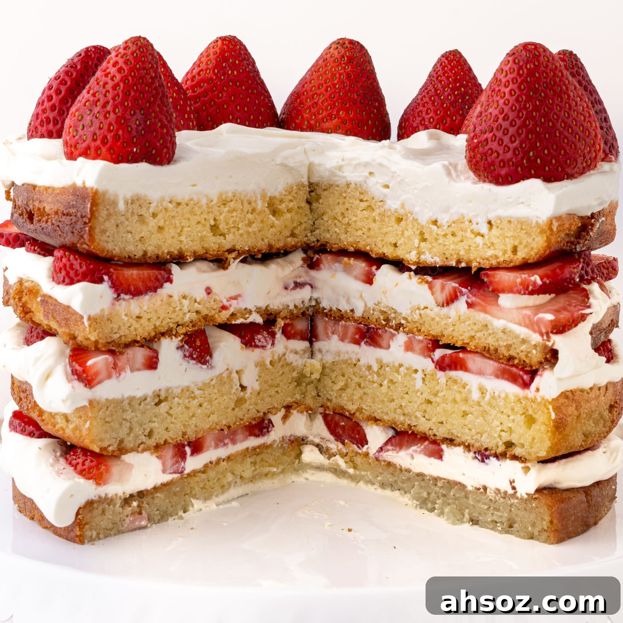 A four layer keto strawberry shortcake sliced with fresh strawberries and whipped cream against a bright white background.