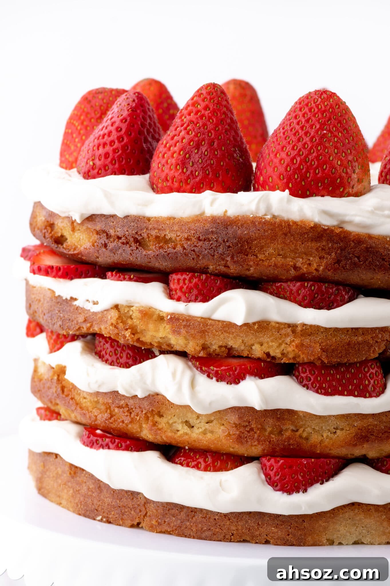 A four layer keto strawberry shortcake with fresh strawberries and whipped cream against a bright white background.