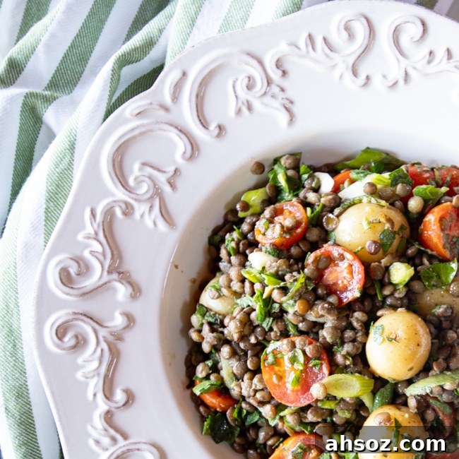 Closeup shot of lentil salad with baby potatoes and tomatoes in a white bowl.