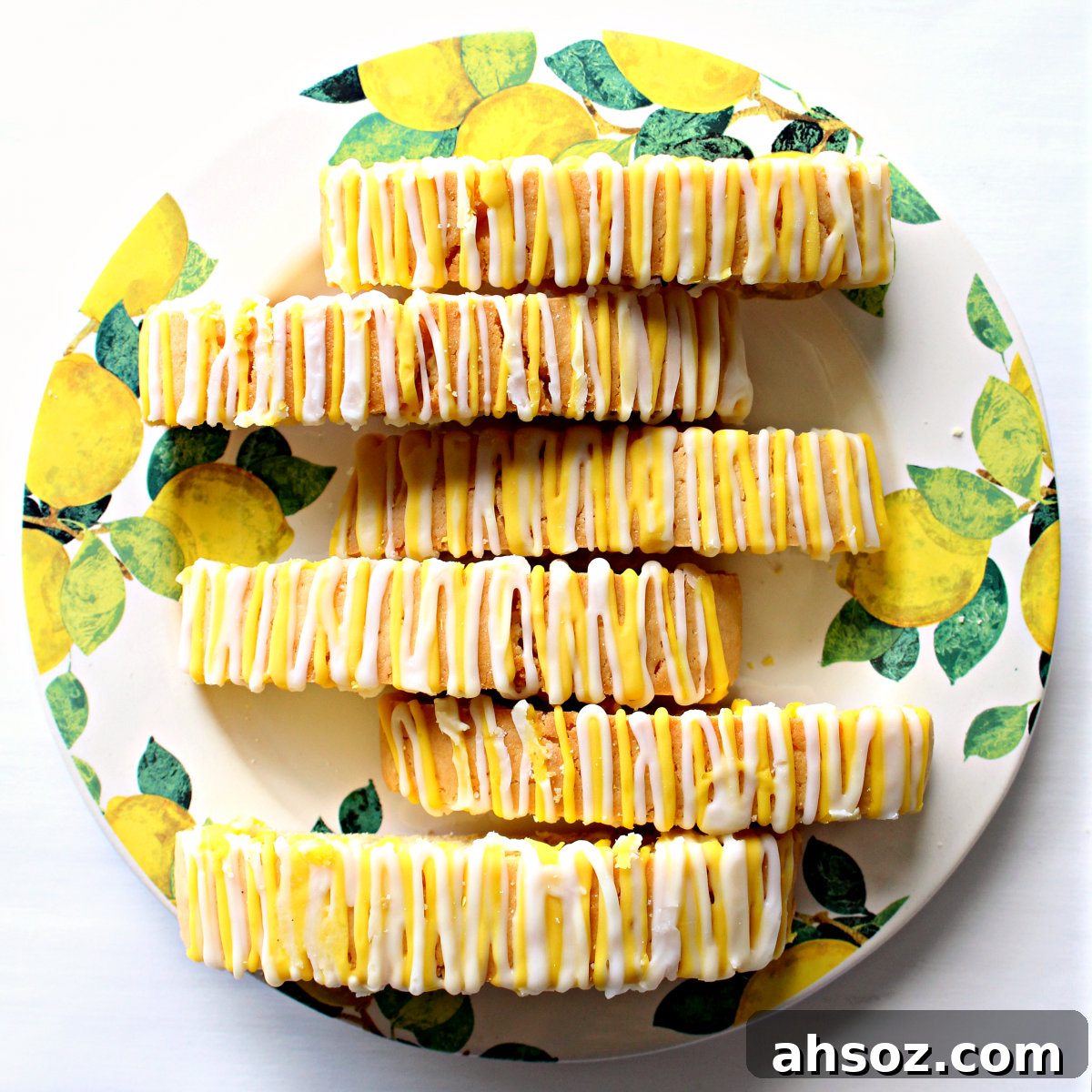 Biscotti with yellow and white icing on a serving plate decorated with images of lemons.