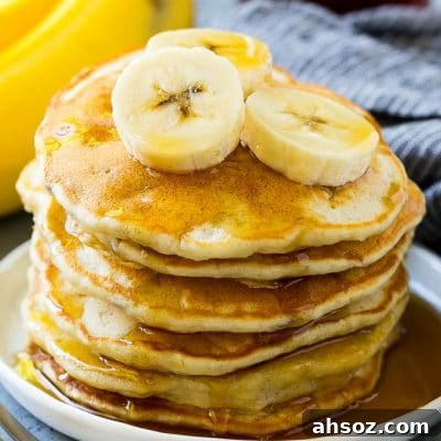 A stack of banana pancakes with banana slices and maple syrup.