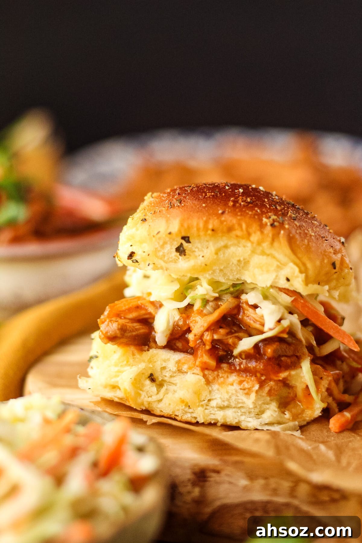 Barbecue pulled chicken sliders with southern coleslaw on a wooden cutting board with a bowl in the background