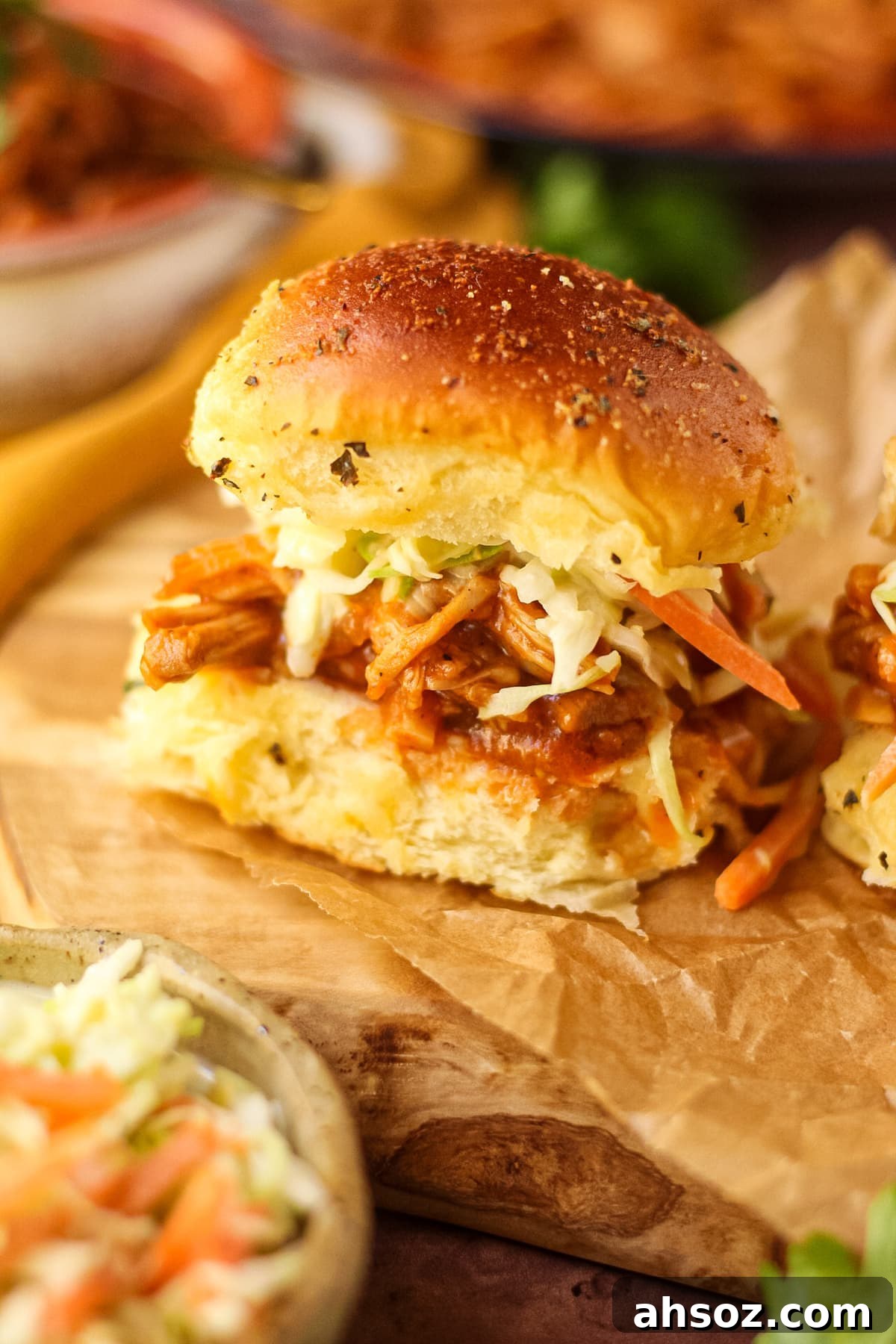 Barbecue pulled chicken sliders with southern coleslaw on a wooden cutting board with a bowl in the background