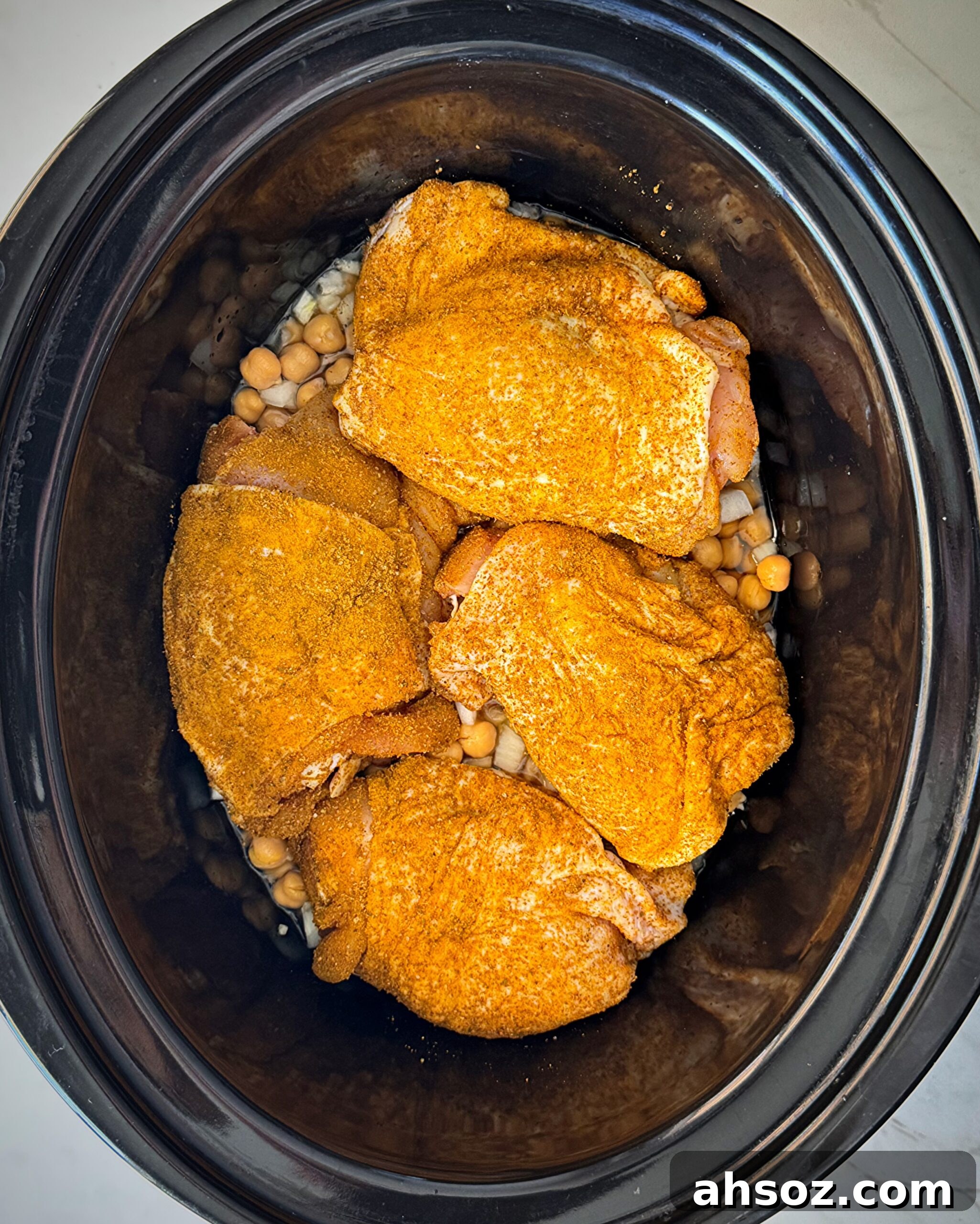 overhead shot of uncooked North African chicken in a black slow cooker
