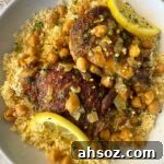 overhead shot of cooked North African chicken on a white plate garnished with fresh parsley & sliced lemon served over couscous
